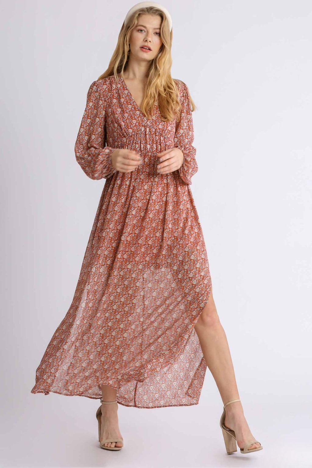 Woman wearing a long, patterned dress with a slit on a white background